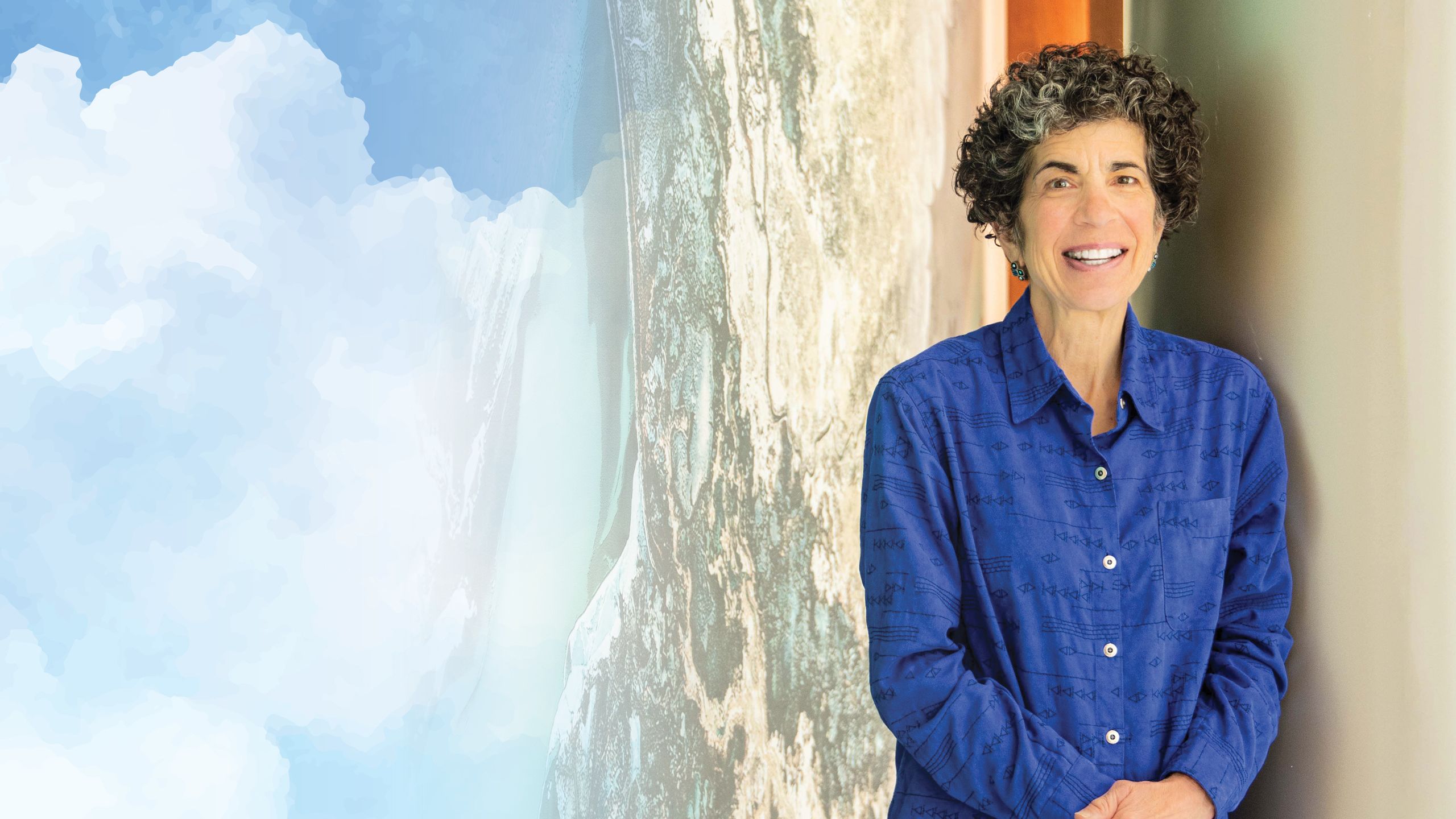 A portrait of an older white woman standing in front of an abstract mural and smiling to the camera.