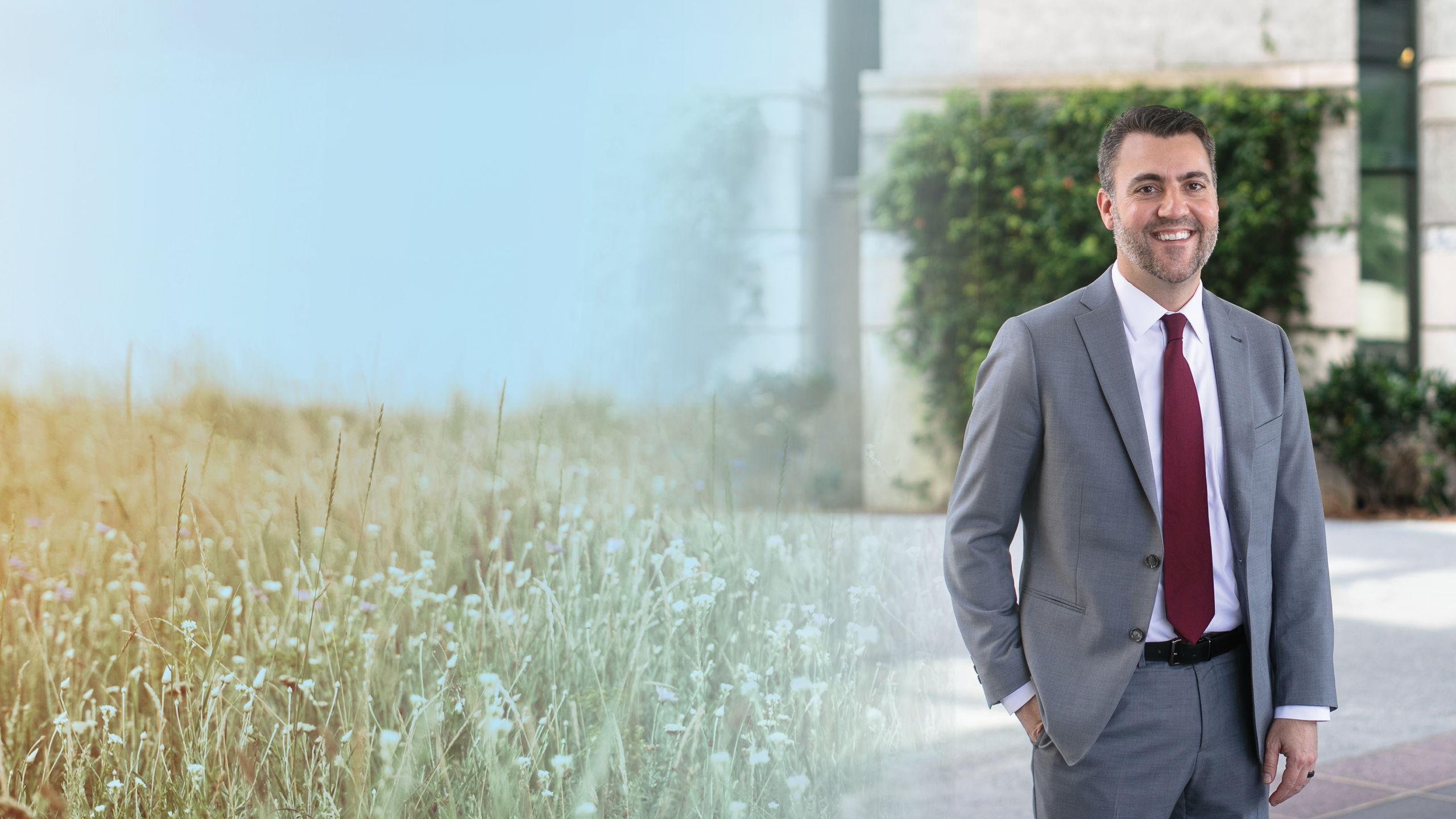 a photo illustration background of a wildflower field on the left and stephen patrick on the right in front of a building with trees and smiling at the camera.