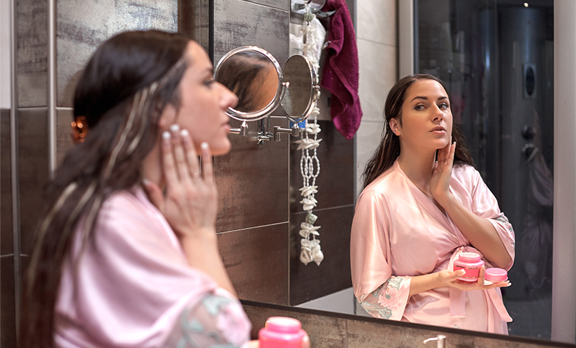 Young pregnant woman with cosmetic cream in a bathroom.