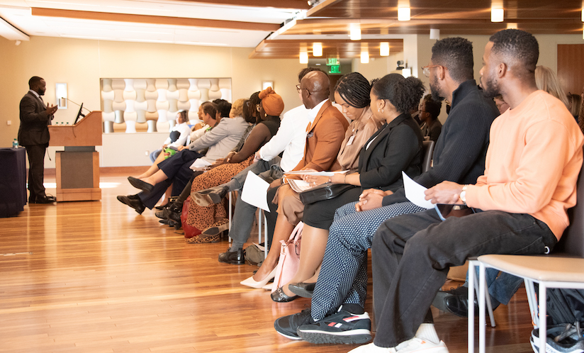 Photo of people sitting in chairs facing a man speaking at a podium
