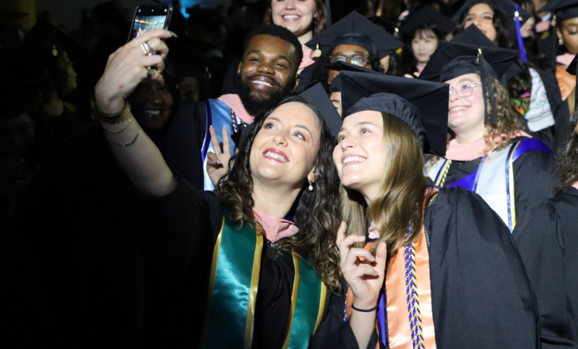 A group of students in master's regalia take a selfie