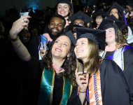 A group of students in master's regalia take a selfie