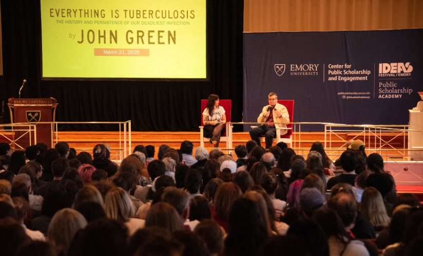 Two people sit on a stage in front of a yellow screen that reads, "Everything is Tuberculosis by John Green"