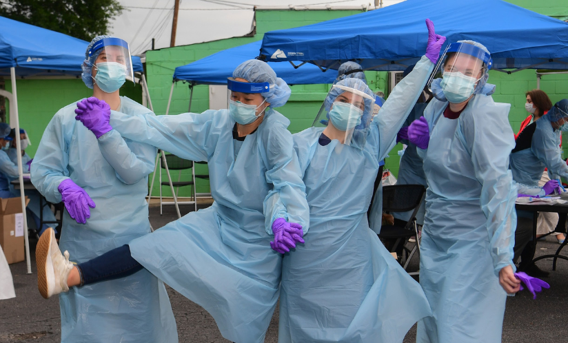 Four public health workers posing in full PPE at a COVID-19 testing site.