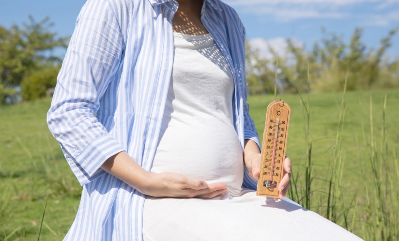 Pregnant woman sitting outside holding a thermometer