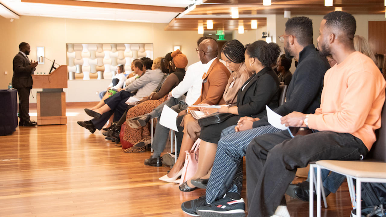 Photo of people sitting in chairs facing a man speaking at a podium