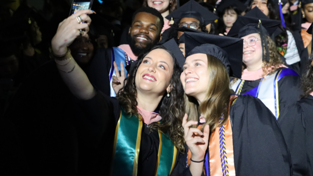 A group of students in master's regalia take a selfie
