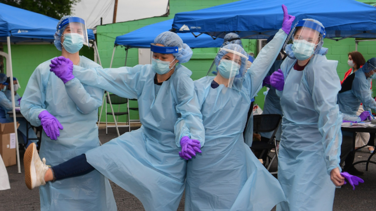 Four public health workers posing in full PPE at a COVID-19 testing site.