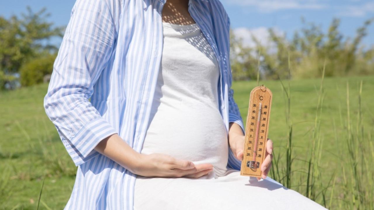 Pregnant woman sitting outside holding a thermometer